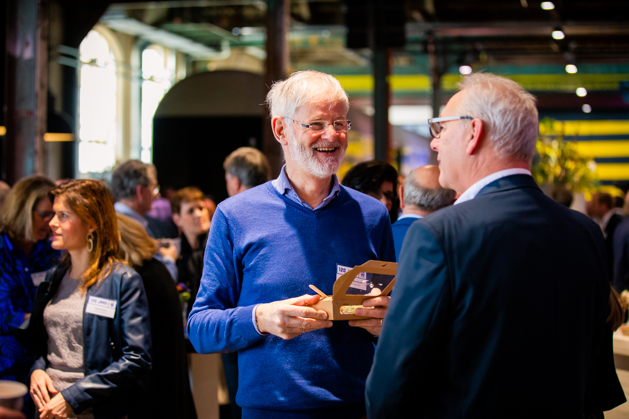 Bezoekers in gesprek tijdens een netwerkmoment op een congres, met ruimte voor ontmoeting en verdieping.